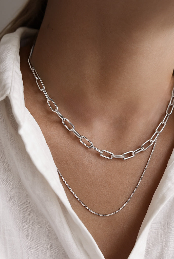 Tjej som bär ett kedjehalsband med ovala länkar kombinerat med en tunn silverkedja.