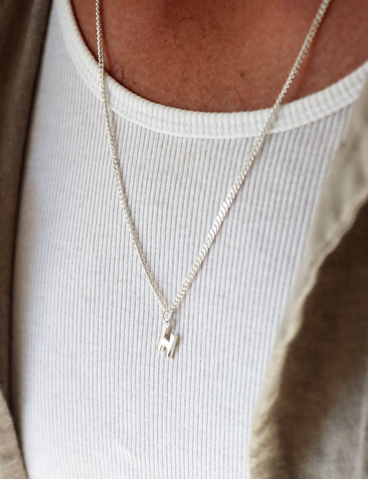 Man som bär ett halsband med bokstav i silverkedja.