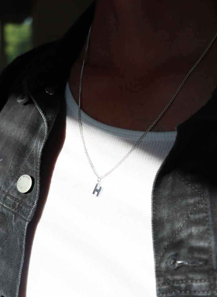 Kille som bär ett silverhalsband med bokstav i pansarkedja.