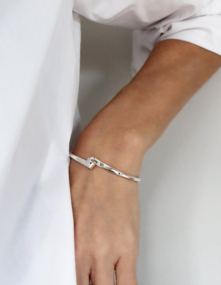 Tjej som bär ett stelt silverarmband i stilren design med en liten loop på framsidan.