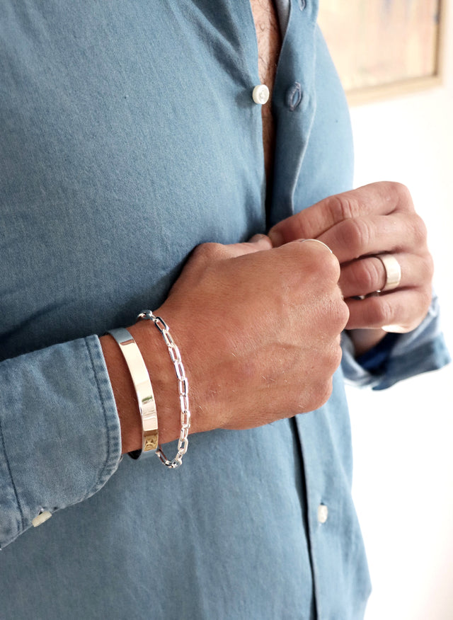 Man som bär ett stelt silverarmband, cuff tillsammans med ett kedjearmband i silver