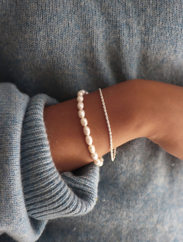 Tjej som bär ett smalt pärlarmband kombinerat med silverarmband.