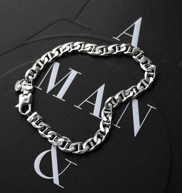 Kedjearmband i silver placerad på svart bakgrund med texten MAN.