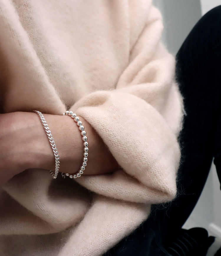 Två silverarmband som bärs i kombination. Ett armband med kulor och ett armband med pansarkedja.