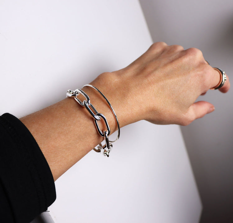 Tjej som bär två silverarmband: en stor silverkedja och ett smalt stelt silverarmband.