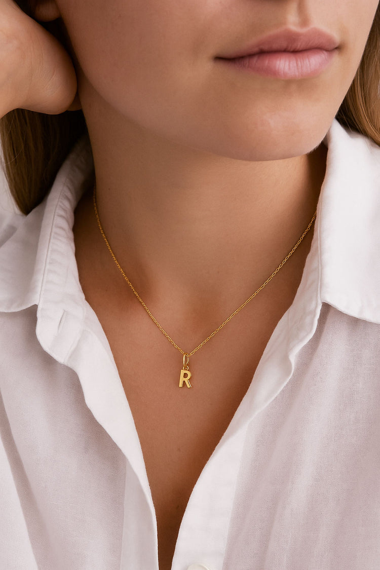 Kvinna i vit skjorta som bär ett bokstavshalsband i guld.