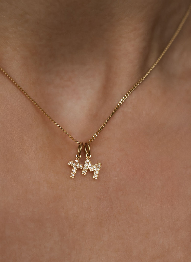 Kvinna som bär ett halsband med ett diamantkors i guld och en bokstavsberlock i guld med diamanter.