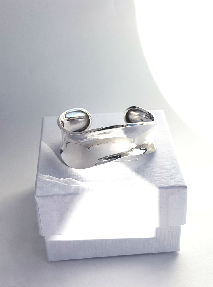 Stelt silverarmband med vågig form placerad på en ask från Mila Silver.