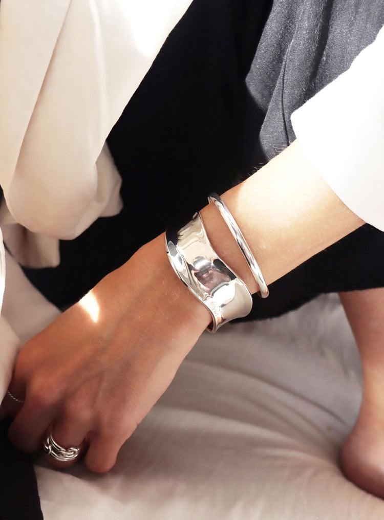 Kvinna som bär ett brett cuff armband i blankt silver och silverringar.