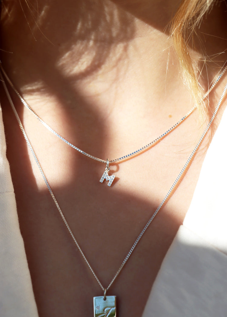 Tjej som bär ett halsband med bokstavsberlock i silver med diamanter