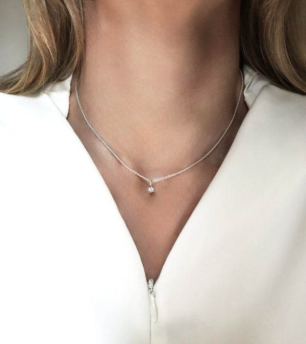Halsband med liten diamant som bärs av en kvinna med vit klädsel.