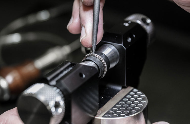 en silversmed infattar diamanter i en ring med ett spetsigt verktyg