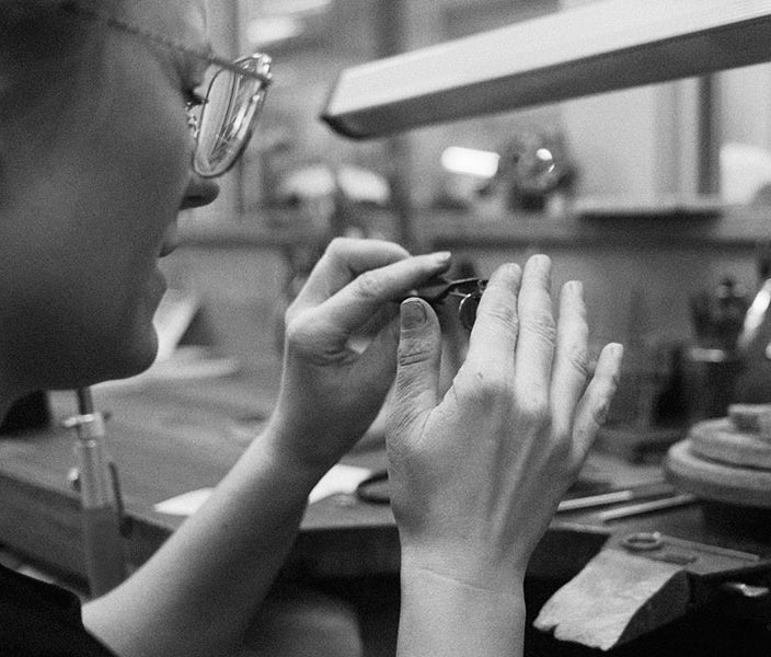 En silversmed i sin verkstad som tillverkar ett diamanthalsband.