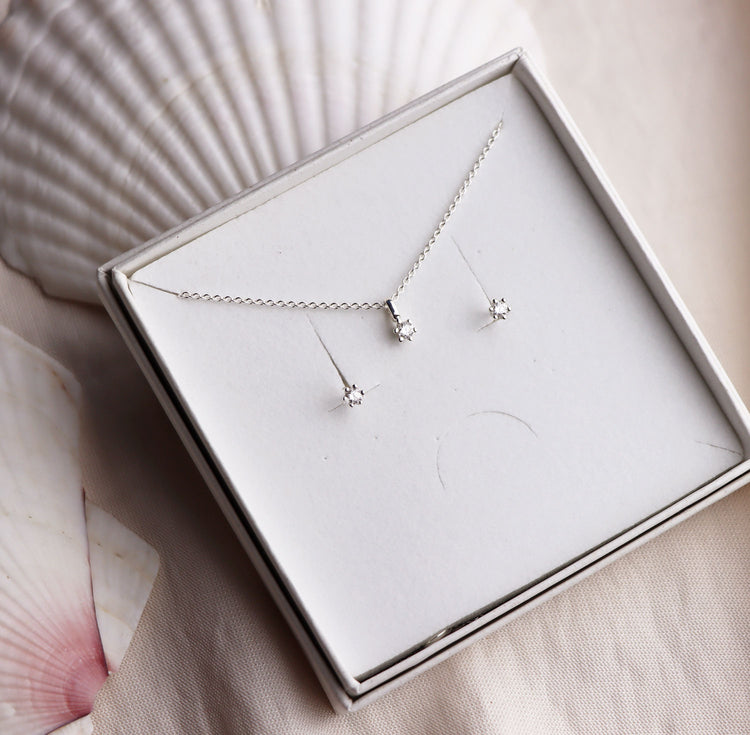 Set med diamanthalsband och diamantörhängen i en vit smycke ask som ligger på två stora snäckor.