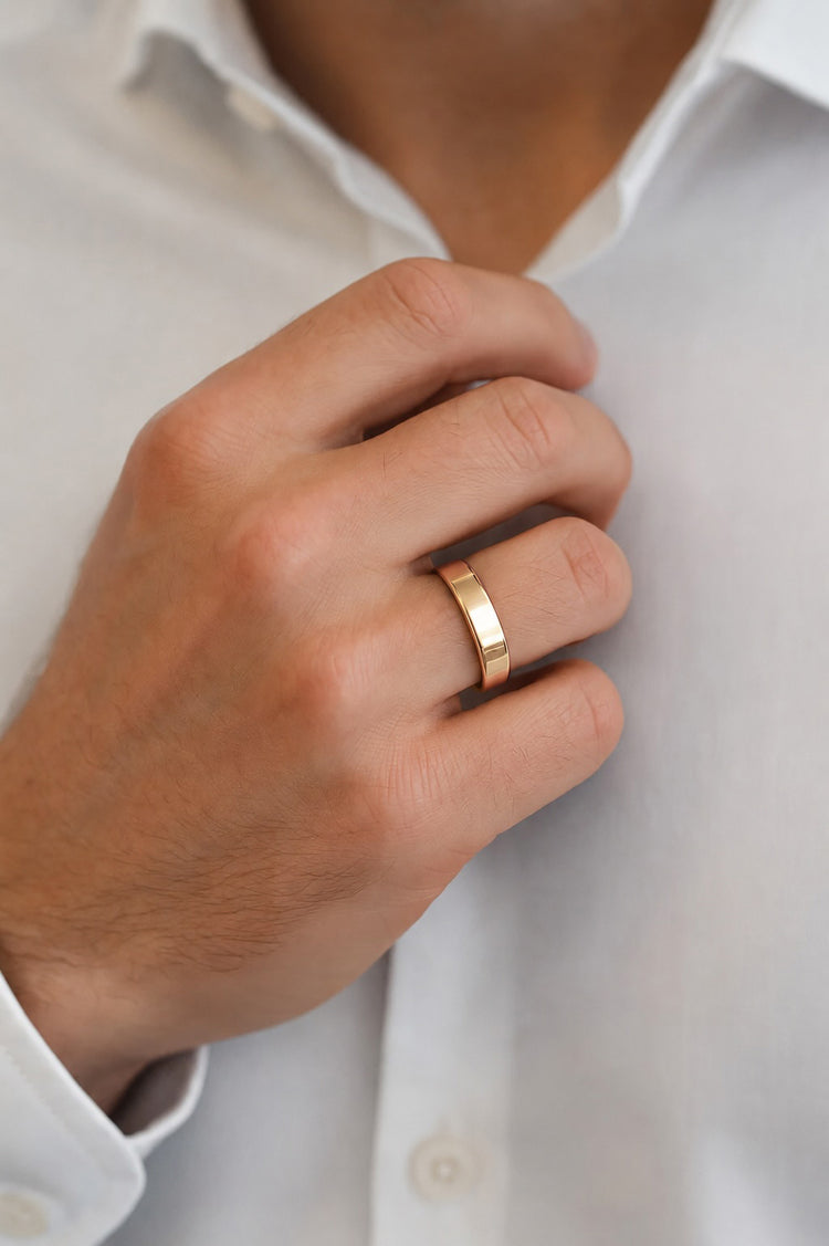 Man som bär en vigselring i guld. Slät ring med raka kanter, 5 mm bred.