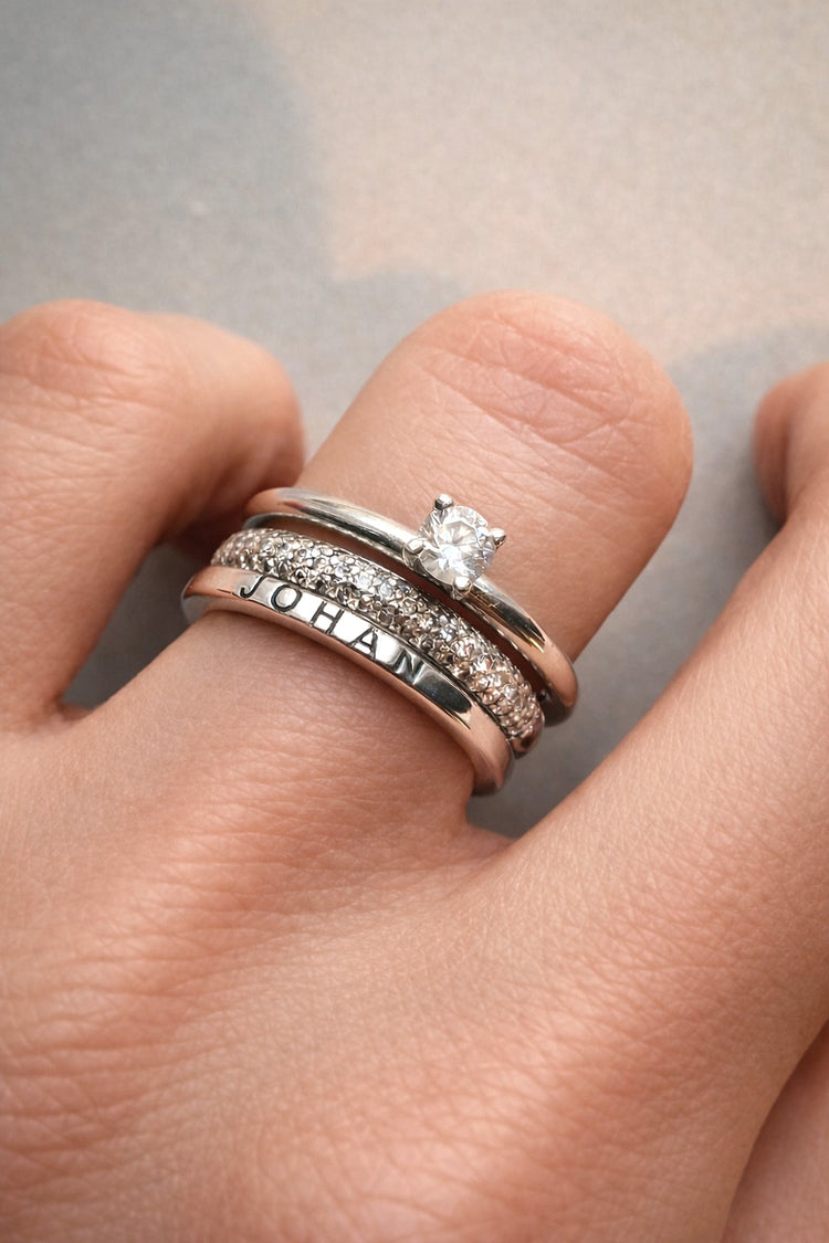 En kvinna som bär en ring med utvändigt graverat namn kombinerad med två diamantringar, vigsel och förlovningsringar.