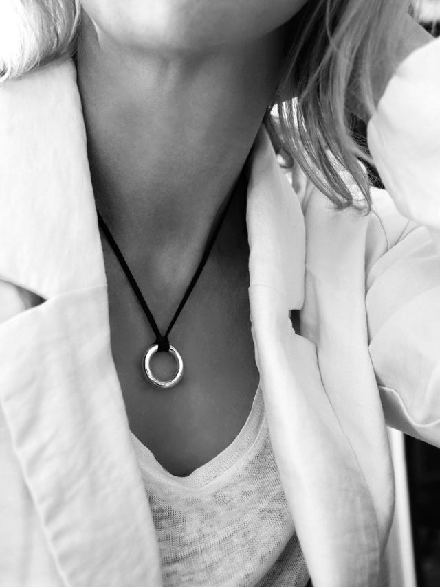 Tjej som bär ett halsband med en silverring i svart läderband. Ringen har graverad text.