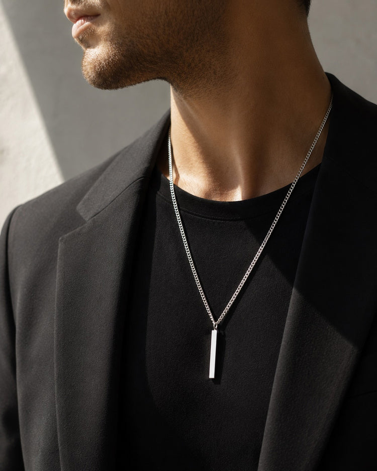 Man som bär ett längre silverhalsband med stav i kedja. han har svart kostym med svart t-shirt under
