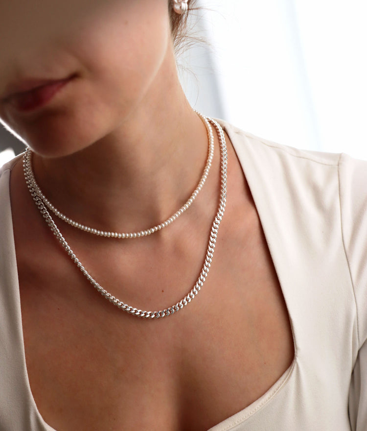 kvinna som bär halsband med 5 mm bred pansar kedja i äkta silver tillsammans med ett kort pärlhalsband