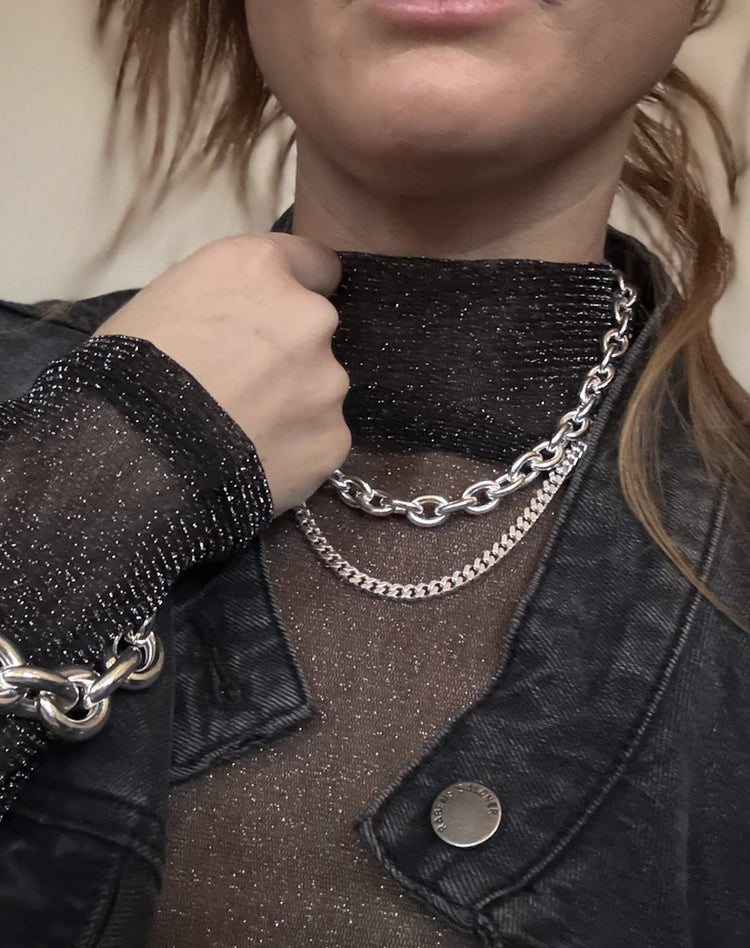 Tjej som bär två halsband med silverkedjor, en pansarkedja och en tjock silverkedja med stora länkar.
