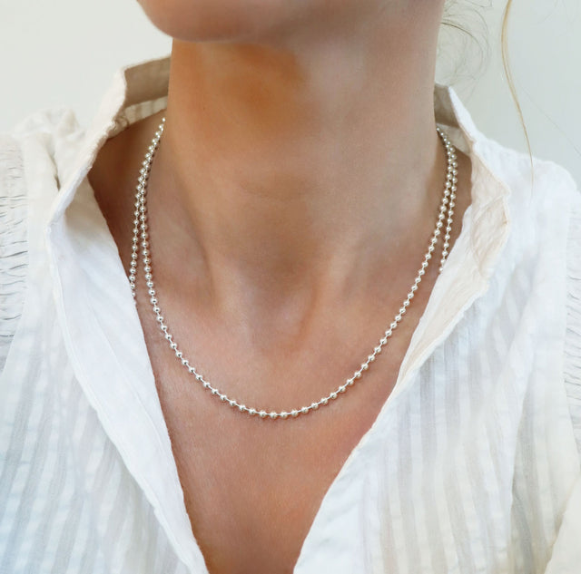 Tjej som bär ett halsband med en silverkedja som har små länkade silverkulor, 45 cm lång. hon bär vit topp.