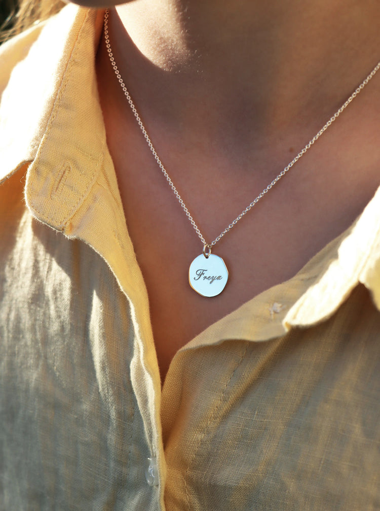 tjej som bär ett halsband med silverberlock som har graverat namn i skrivstil.