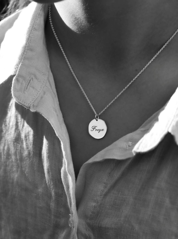 tjej som bär ett halsband med silverberlock som har graverat namn i skrivstil.