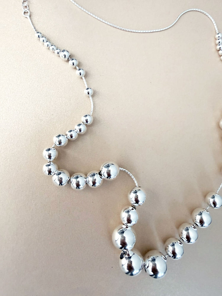 Halsband med silverkulor i olika storlekar som är trädda på en vajer.