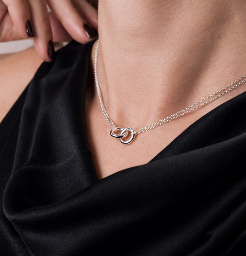Kort silverhalsband med två ringar i kedjor på kvinna som bär svart sidentopp.