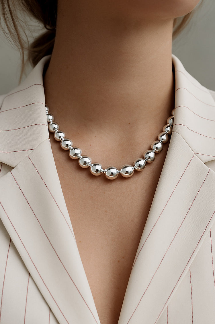 tjej som bär ett halsband med stora silverkulor till vit kavaj .