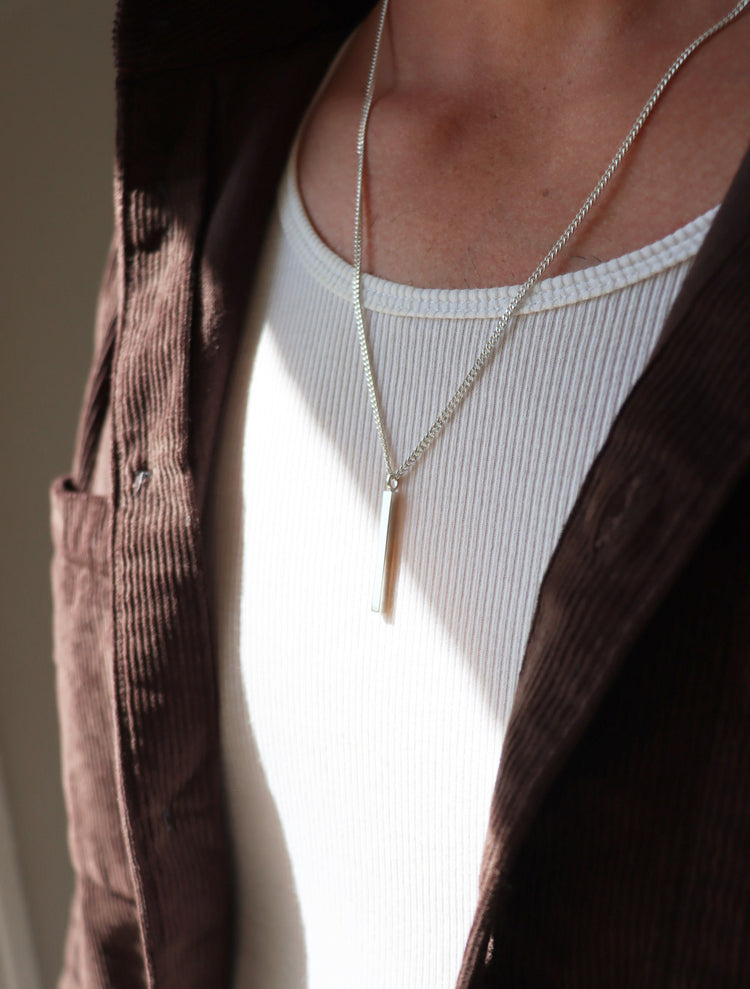 Man som bär ett långt silverhalsband med stav i kedja.
