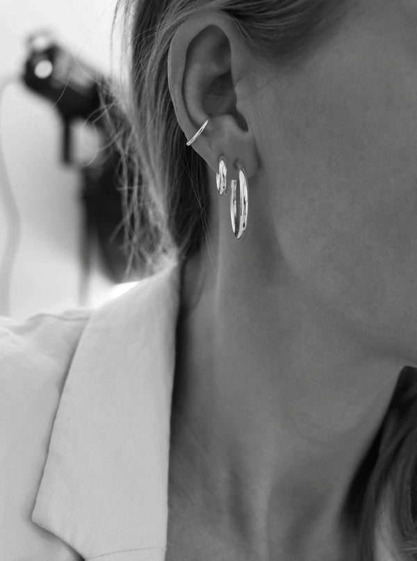 Tjej som bär två silver hoop ringar i samma öra kombinerat med en ear cuff i silver.