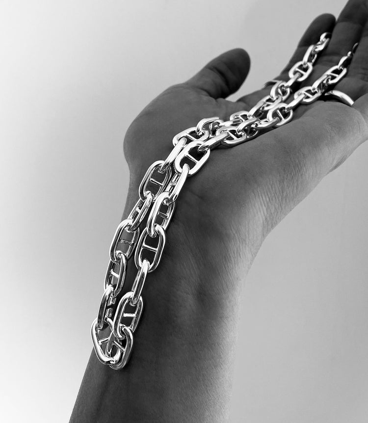 en hand som håller i en grov silverkedja med Ankar-länkar.