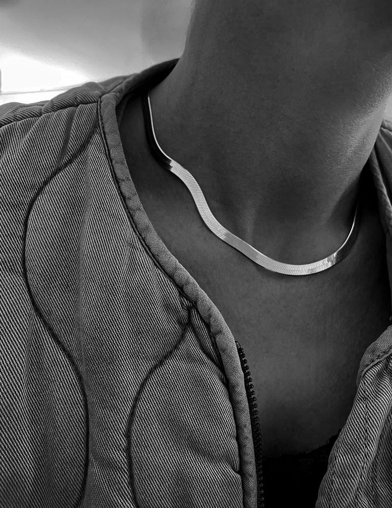 Tjej som bär en platt ormkedja i silver med fin lyster. kedjan är 5 mm bred och kort runt halsen.