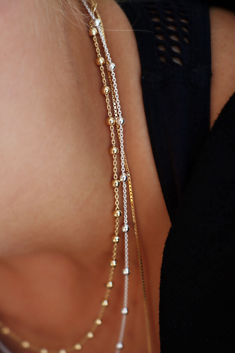 Närbild på guld- och silverkedjor med små kulor.