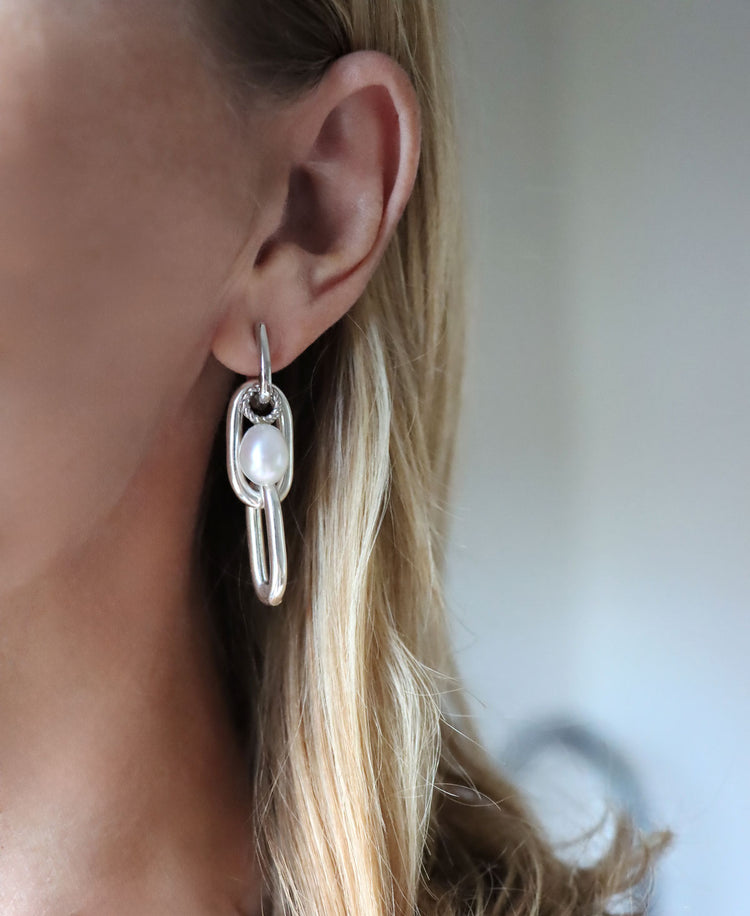 Tjej som bär hängande silverörhängen med kedjor och pärlor.