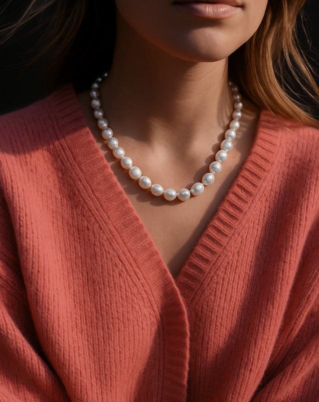 tjej som bär ett pärlhalsband med stora vita pärlor till korallfärgad stickad tröja.