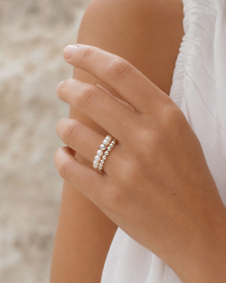 Tjej som bär en pärlring tillsammans med en silverring som har silverkulor.