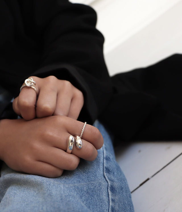 Tjej som bär en stor silverring som går omlott på fingret. Hon bär fler silverringar på de andra fingrarna.