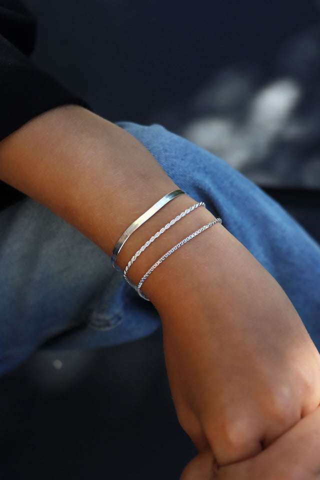 Tjej som bär tre smala silverarmband i kombination. Rope kedja, Box kedja och Snake kedja.