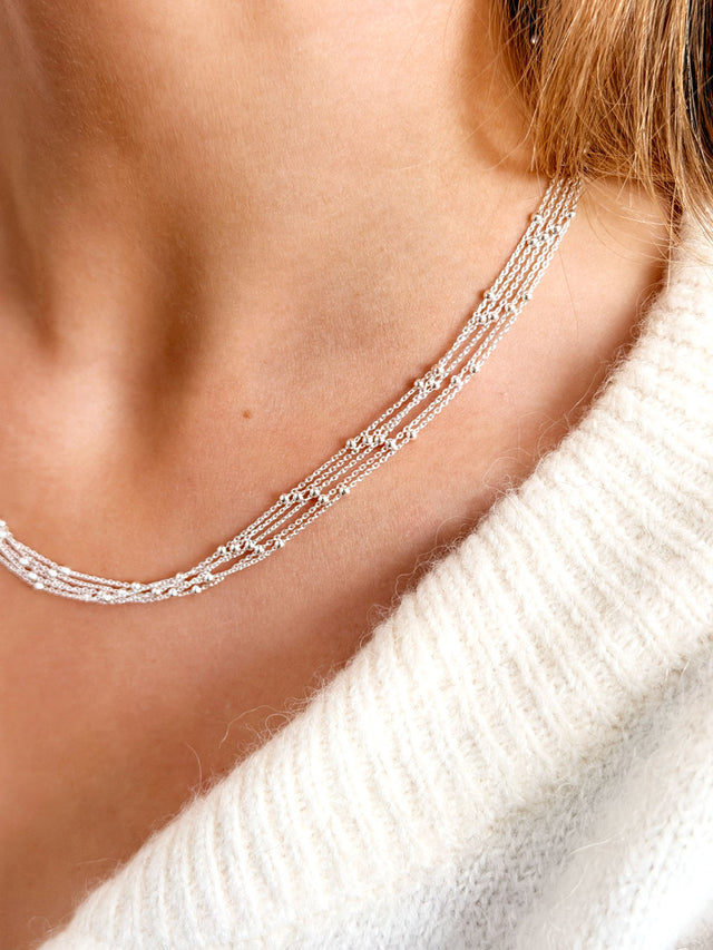 Tjej som bär ett kort halsband i silver med tunna kedjor och små silverkulor.