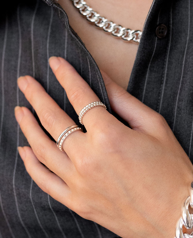 Tjej som bär två smala ringar med kulor på pekfingret kombinerat med två smala silverringar på långfingret.