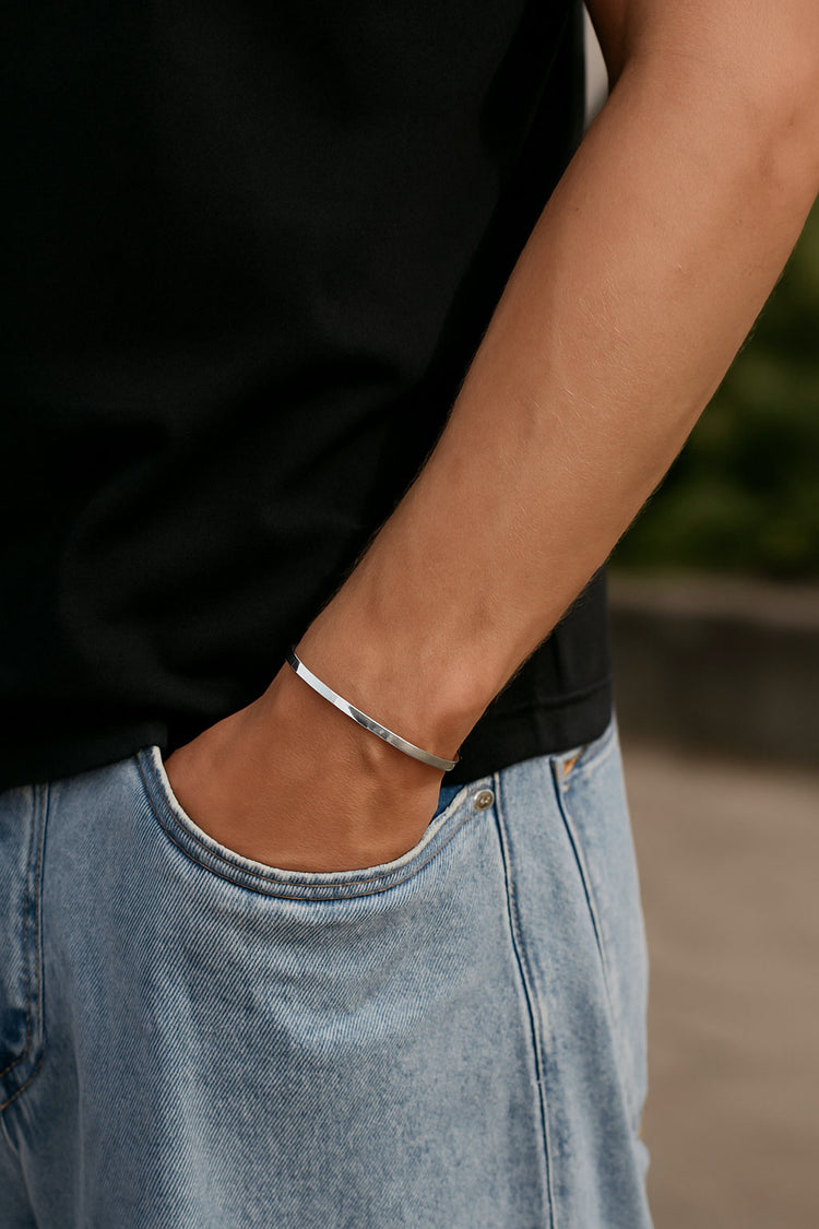 Kille som bär ett smalt stelt silverarmband med blank yta.