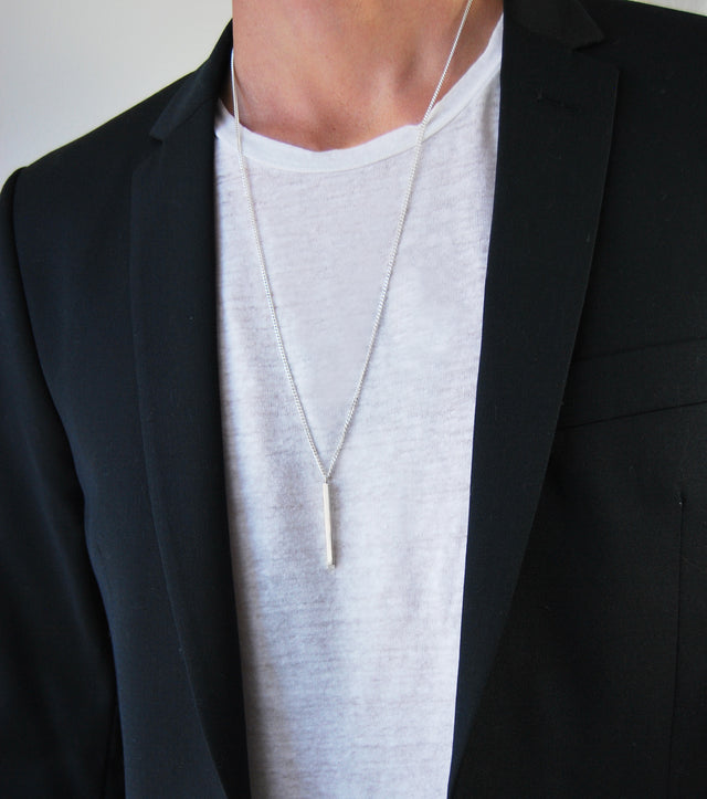 Man som bär ett långt silverhalsband med en silverstav i kedja.