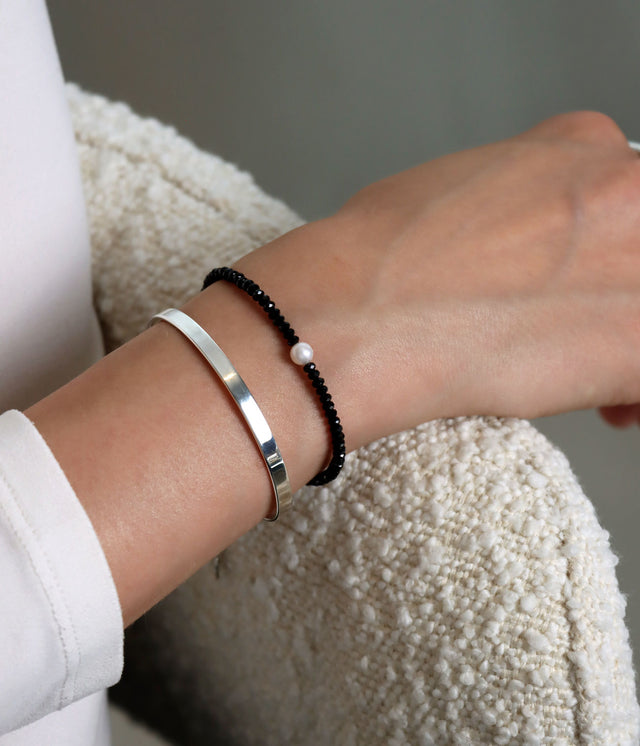 Tjej som bär ett armband med svarta stenar tillsammans med ett stelt silverarmband