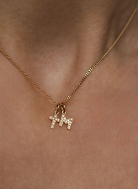 Kvinna som bär ett halsband med ett diamantkors i guld och en bokstavsberlock i guld med diamanter. 