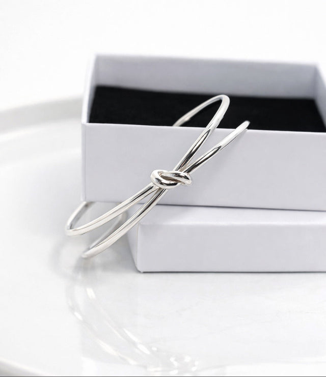 Stelt silverarmband med knut placerat på en vit smyckesask. 