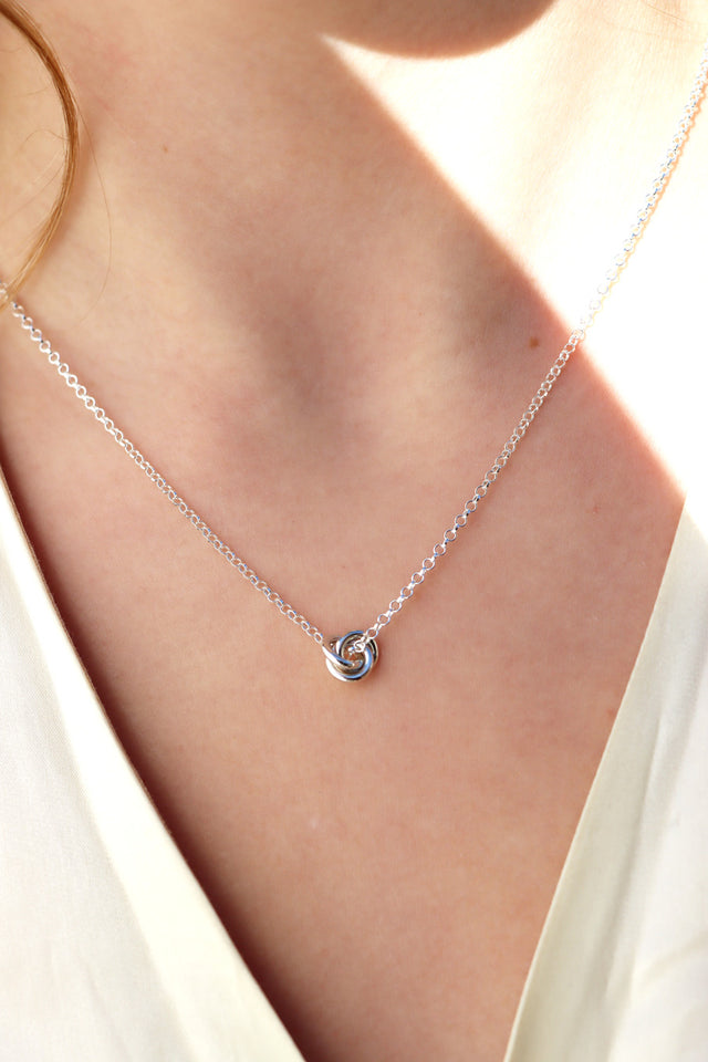 Tjej som bär ett silverhalsband med en liten knut. 