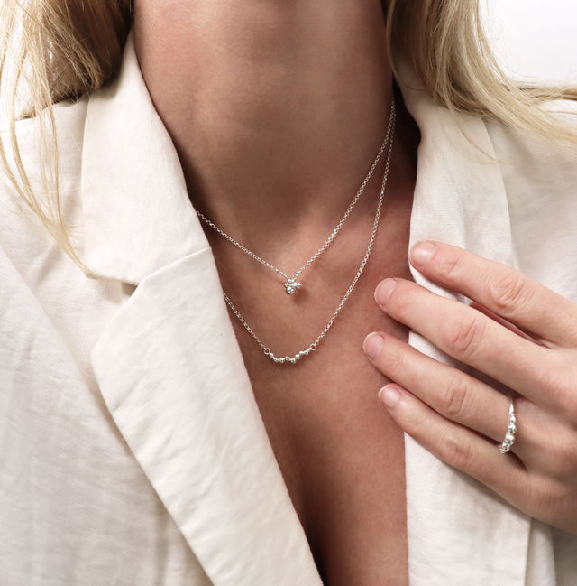 Tjej som bär två silverhalsband och silverring med små kulor. 