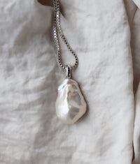 Halsband med stor pärla som har ojämn form placerad på ett mjukt tyg. 